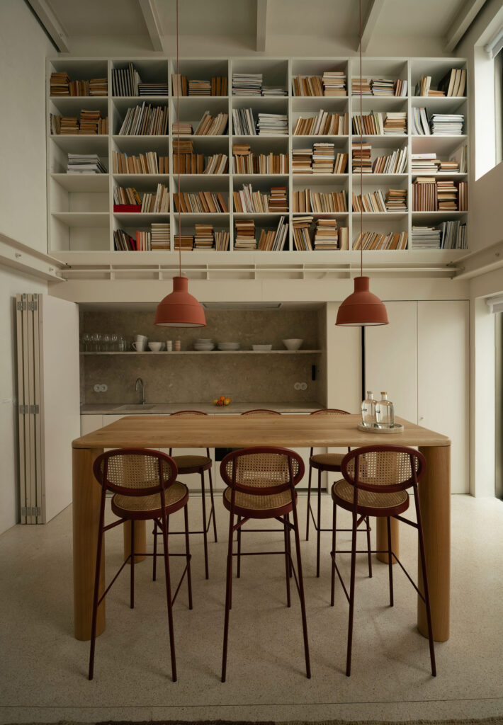 Kitchen and dining table under a double-height bookshelf – LIOZ Lisboa