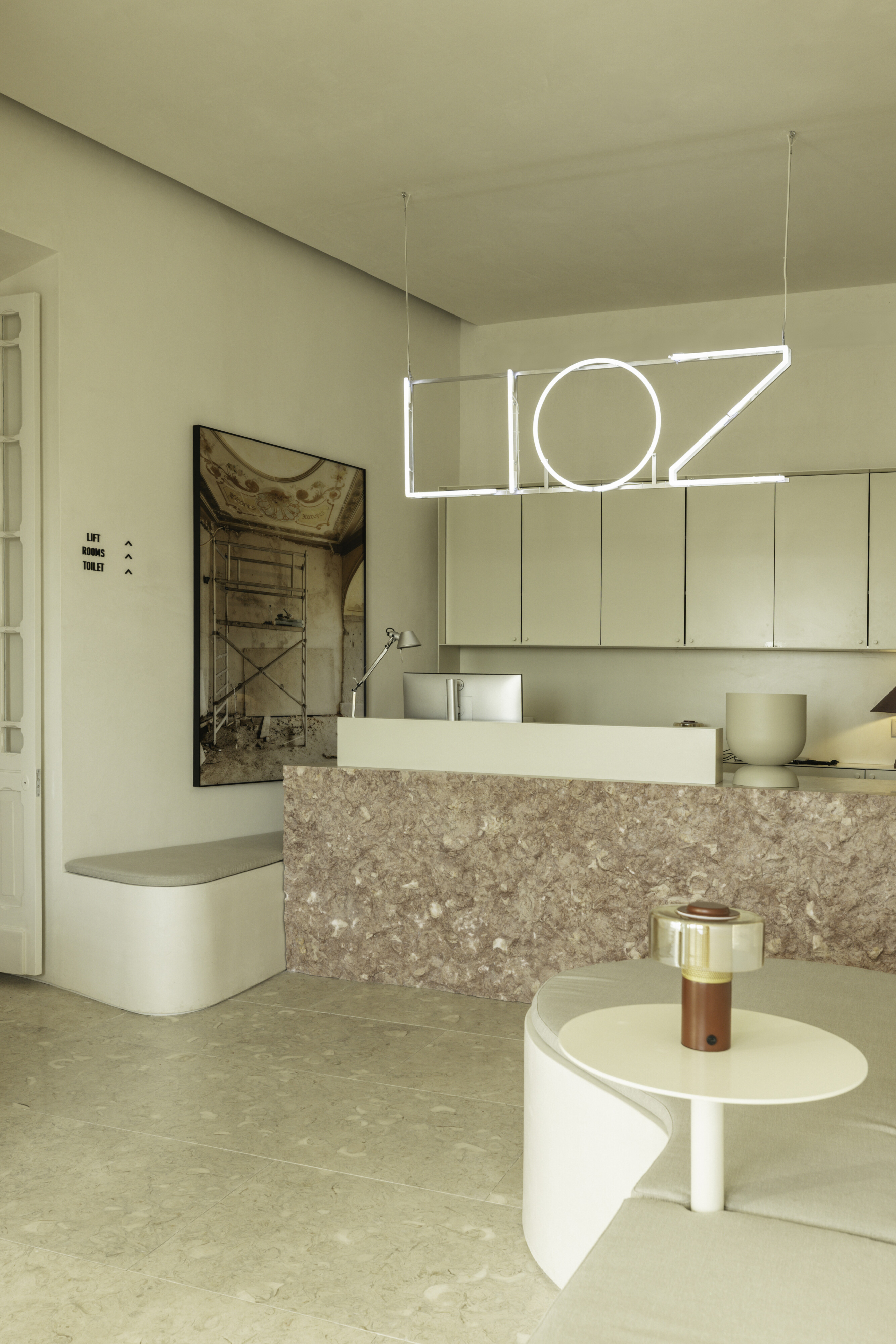 The reception at LIOZ Lisboa, with the LIOZ neon sign above a pink stone counter